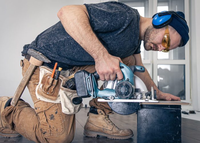 Building contractor worker using hand held worm drive circular saw to cut boards on a new home constructiion project.