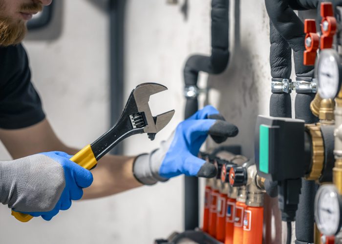 A man installs a heating system in a house and checks the pipes with a wrench. Adjusting heating valves in a residential building. A plumbing and heating technician works.